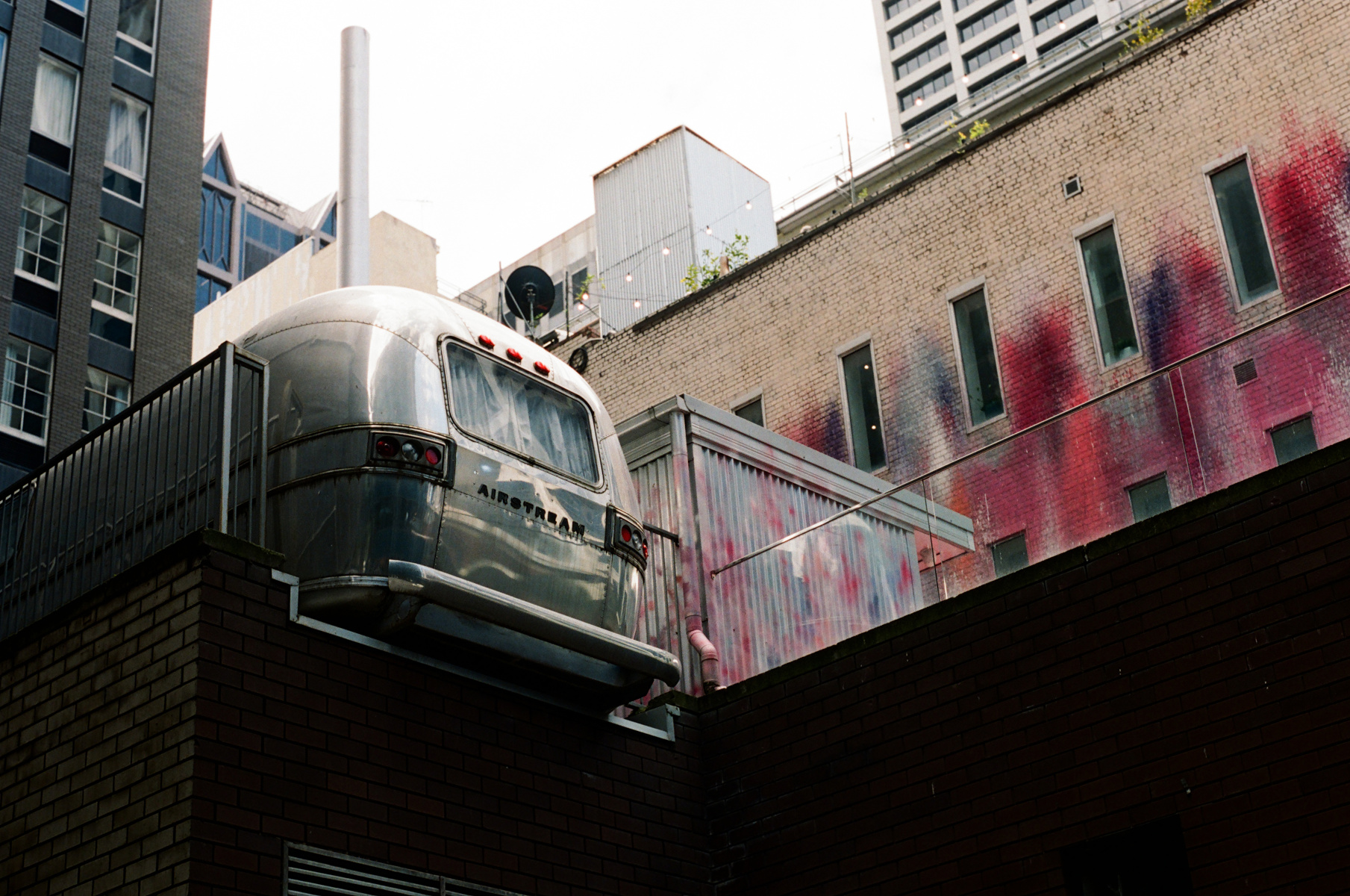 Colour photograph of an Airstream caravan/trailer sitting atop a garage in a city laneway, with paint-splattered walls in the background